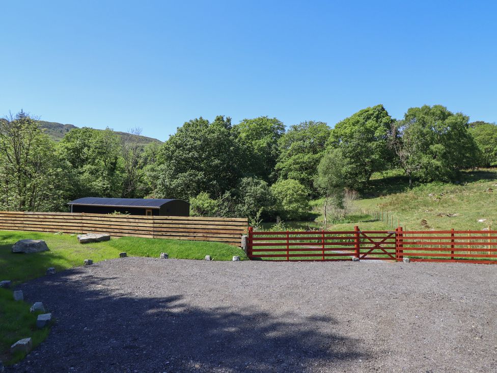 An outdoor scene with a gravel area a wooden fence a red gate and trees at Celyn in Bontddu near Dolgellau