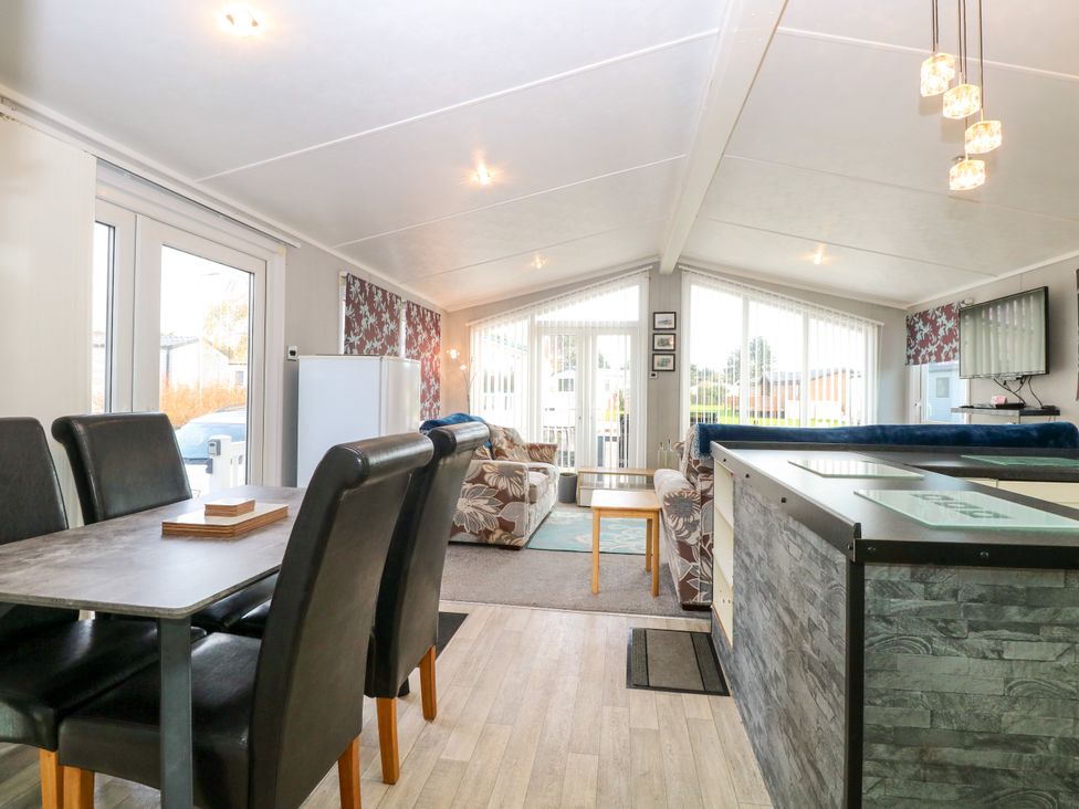 An open living room and dining area with a dining table and chairs a sofa a television and large windows at 3 Bure Close Burgh Castle