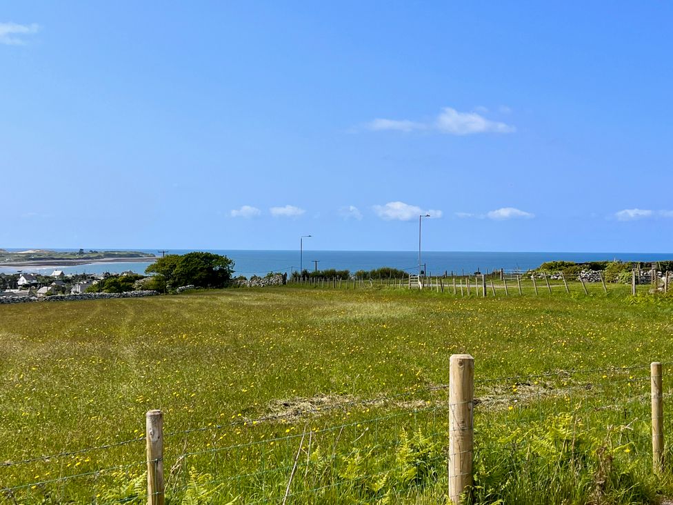 A fenced grass field with wildflowers and a view of the ocean in the distance at Glynmor in Llandanwg near Harlech