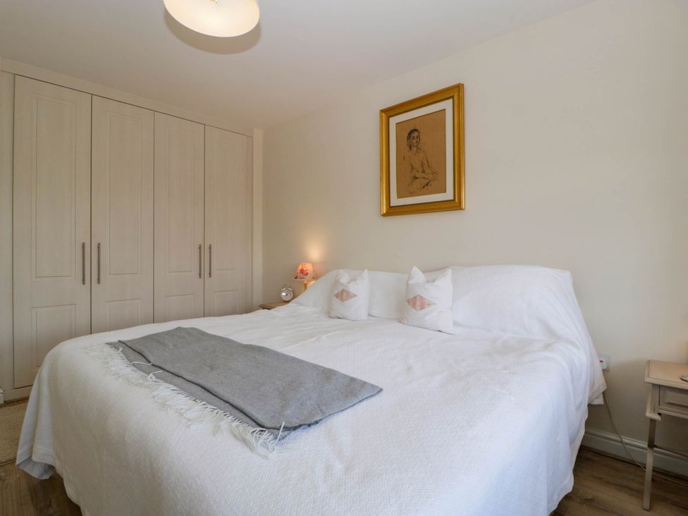 A bedroom with a double bed with white bedding and pillows a gray throw a wooden wardrobe bedside tables with lamps and a framed picture on the wall at Bridge View in Sudbrook near Caldicot