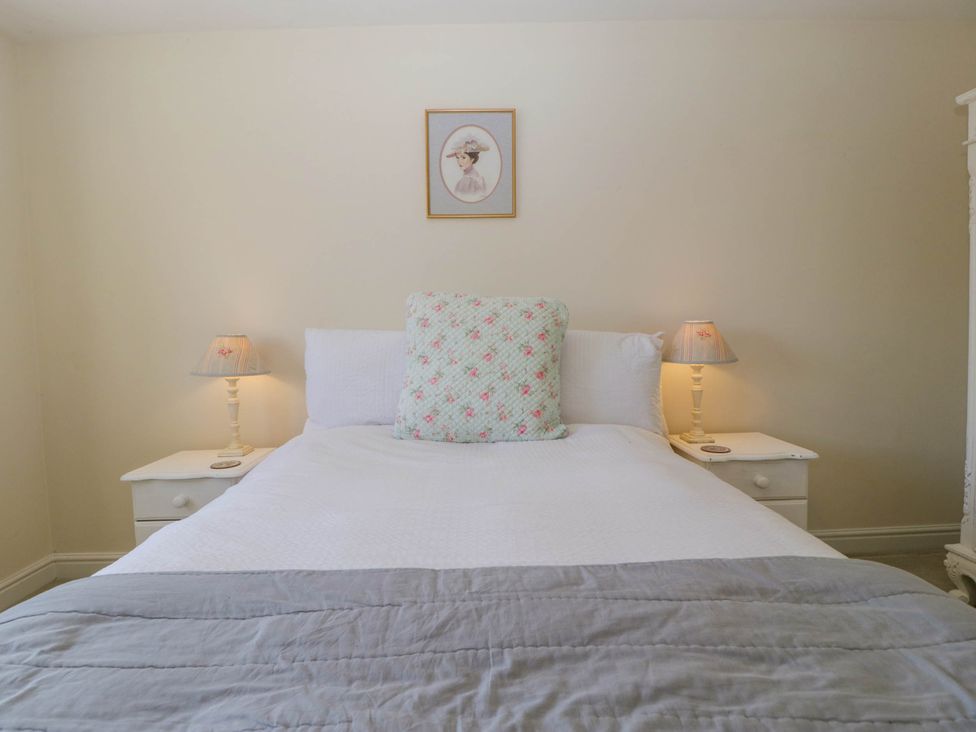 A bedroom with a white bed having a floral cushion and two bedside tables with lamps at Bridge View in Sudbrook near Caldicot