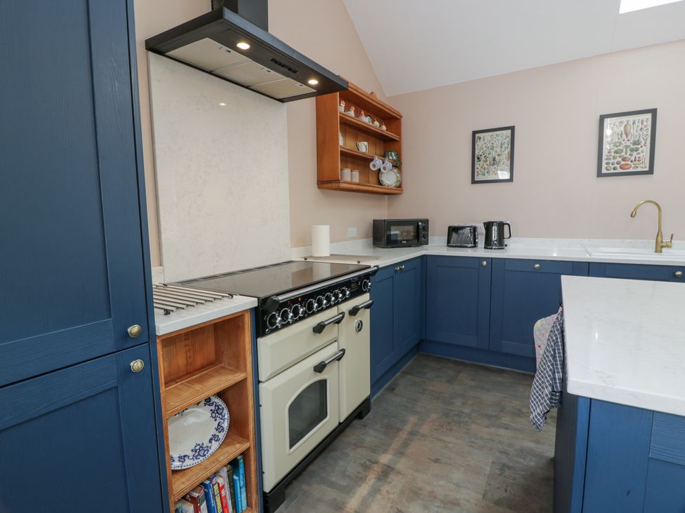 A kitchen with blue cabinets a stove microwave toaster kettle and framed pictures on the wall at Morton Mains Steading Cottage Near Thornhill