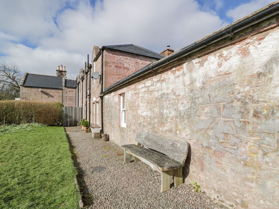 A stone building with a wooden bench on a gravel path next to a grassy lawn at Morton Mains Steading Cottage Near Thornhill
