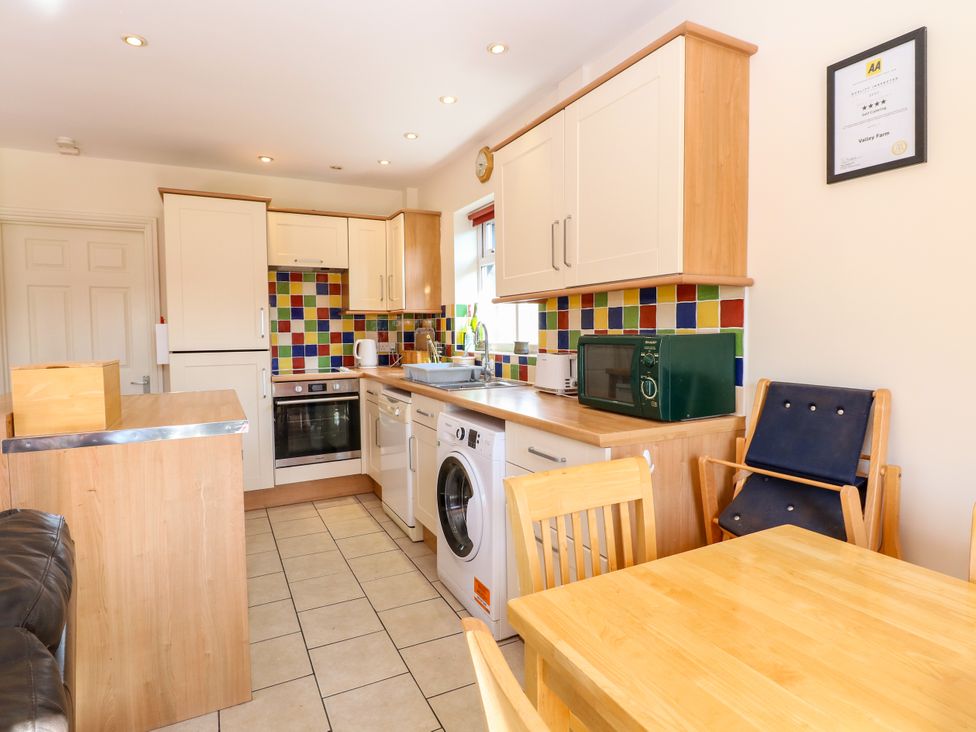 A kitchen with wooden cabinets colorful tiled backsplash appliances and a wooden dining table with chairs at Swallow Barn in Holton near Halesworth