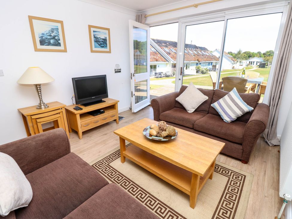 A living room with brown sofas a wooden coffee table a television on a wooden stand and sliding glass doors leading outside at Cape 12 Near Yarmouth