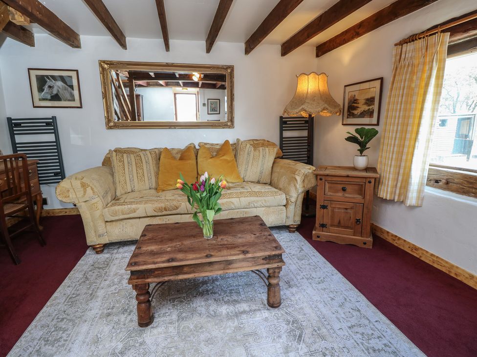 A living room with a beige patterned sofa with three mustard cushions a wooden coffee table with flowers a wooden side table with a plant and a lamp and yellow checked curtains at The Granary Hill Farm near Freshwater