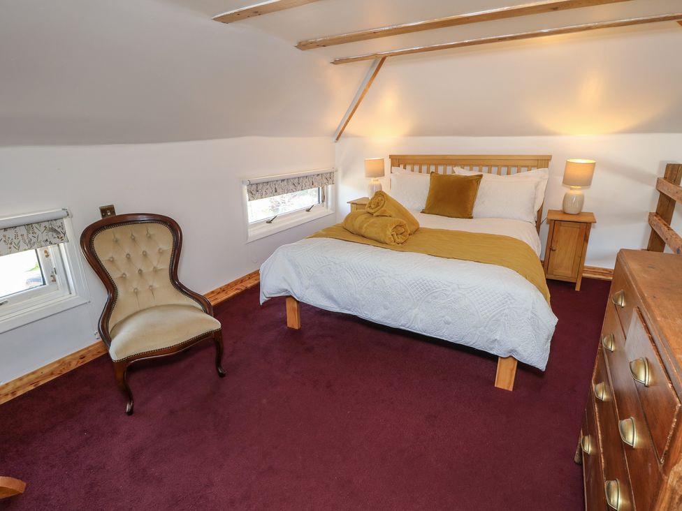 A bedroom with a bed, two bedside tables with lamps, an upholstered chair, and a wooden chest of drawers at The Granary Hill Farm near Freshwater