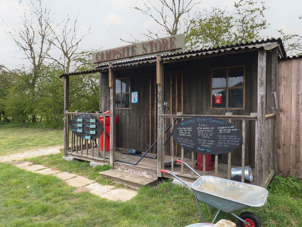 A small wooden campsite store with signs and a wheelbarrow outside at Bluebelle (Cow Shed 5) in Easton near Campsea Ashe