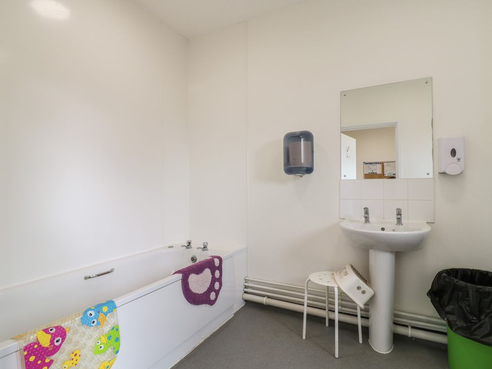 A bathroom with a bathtub a sink a mirror a stool a trash bin and soap dispensers at Bluebelle Cow Shed 5 Easton near Campsea Ashe