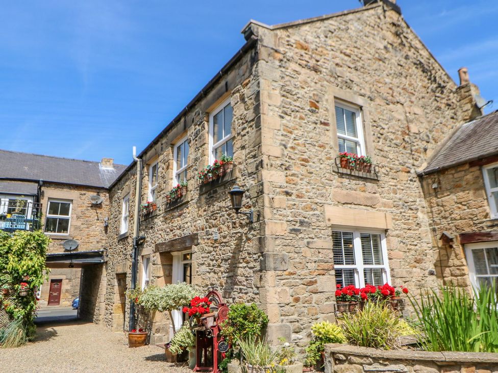 A stone building with multiple windows and flower boxes outside a courtyard at Shaftoe Mews in Haydon Bridge