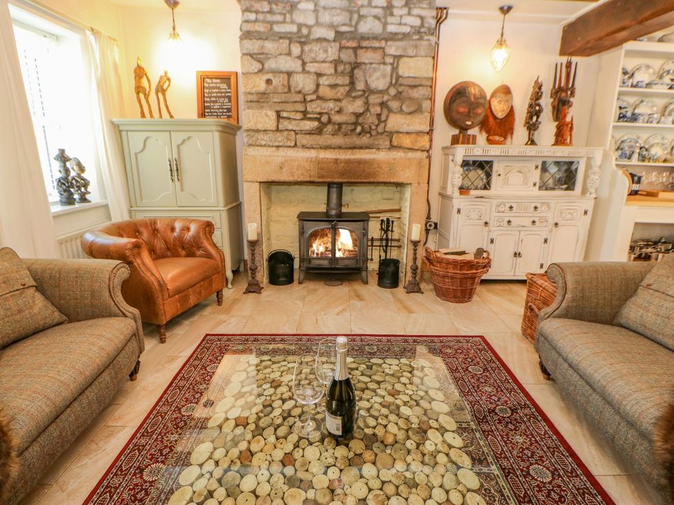 A living room with a stone fireplace leather and fabric sofas a glass coffee table with wine bottle and glasses at Shaftoe Mews in Haydon Bridge