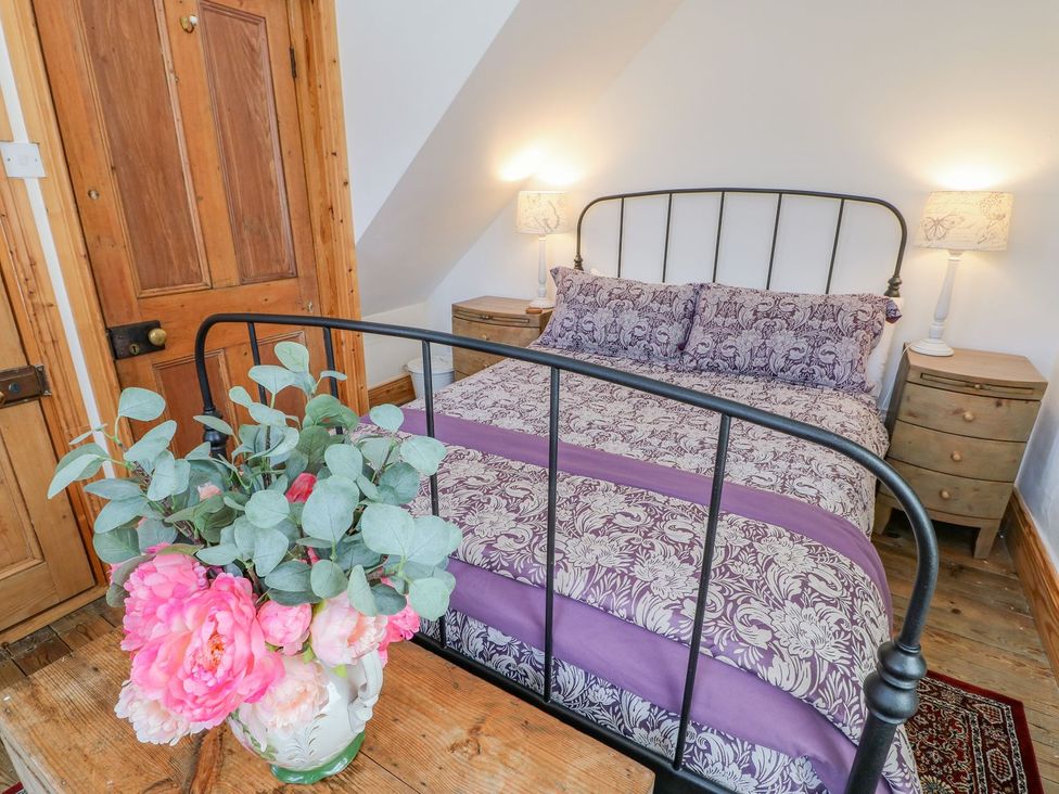 A bedroom with a metal bed frame and floral bedding beside two wooden nightstands with lamps at Shaftoe Mews in Haydon Bridge