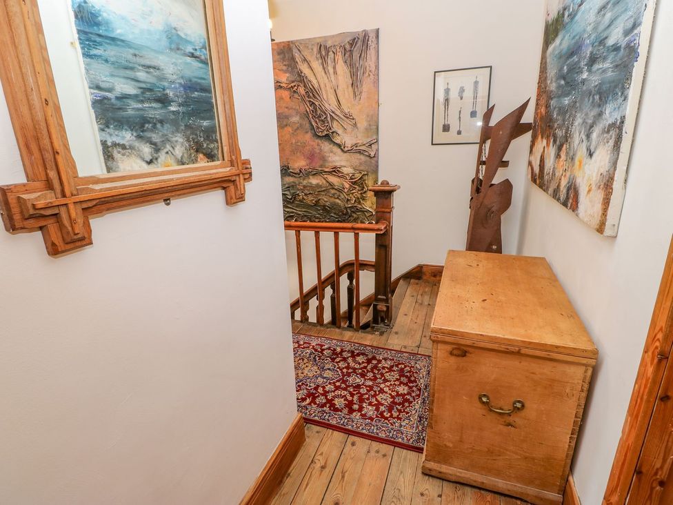A hallway with wooden stairs a wooden chest a red patterned rug and several wall paintings at Shaftoe Mews in Haydon Bridge