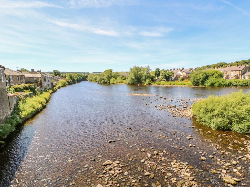 A river with stone houses and greenery on both banks at Shaftoe Mews in Haydon Bridge