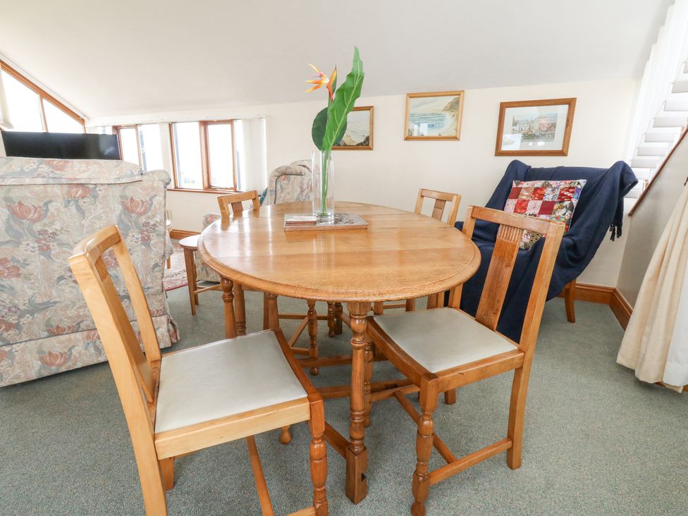 A dining area with a round wooden table and four wooden chairs a vase with a flower on the table a living room area with floral sofas and framed pictures on the wall at Old Higher Lighthouse Branscombe Lodge Portland Bill