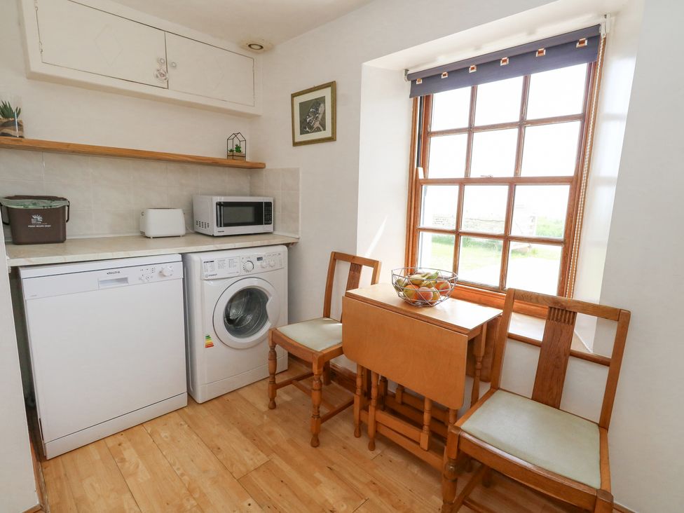 A small kitchen area with a dishwasher washing machine wooden table chairs and a window at Old Higher Lighthouse Branscombe Lodge Portland Bill