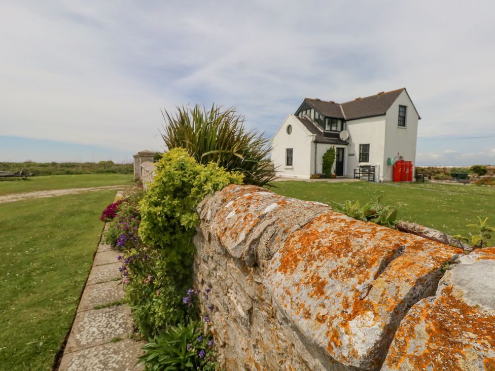 A stone wall with plants and flowers beside a white house with a pitched roof at Old Higher Lighthouse Branscombe Lodge Portland Bill