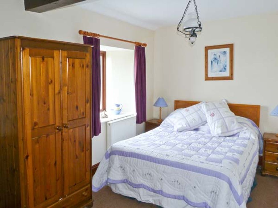 A bedroom with a wooden wardrobe bed with white and purple bedding bedside tables and purple curtains at The Carthouse in Shorwell