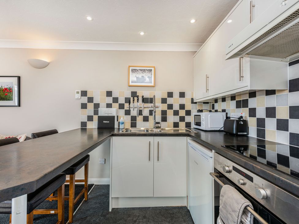 A kitchen with a countertop and stools a sink a microwave a toaster an oven and a tiled backsplash at 16 The Boathouse in Rye