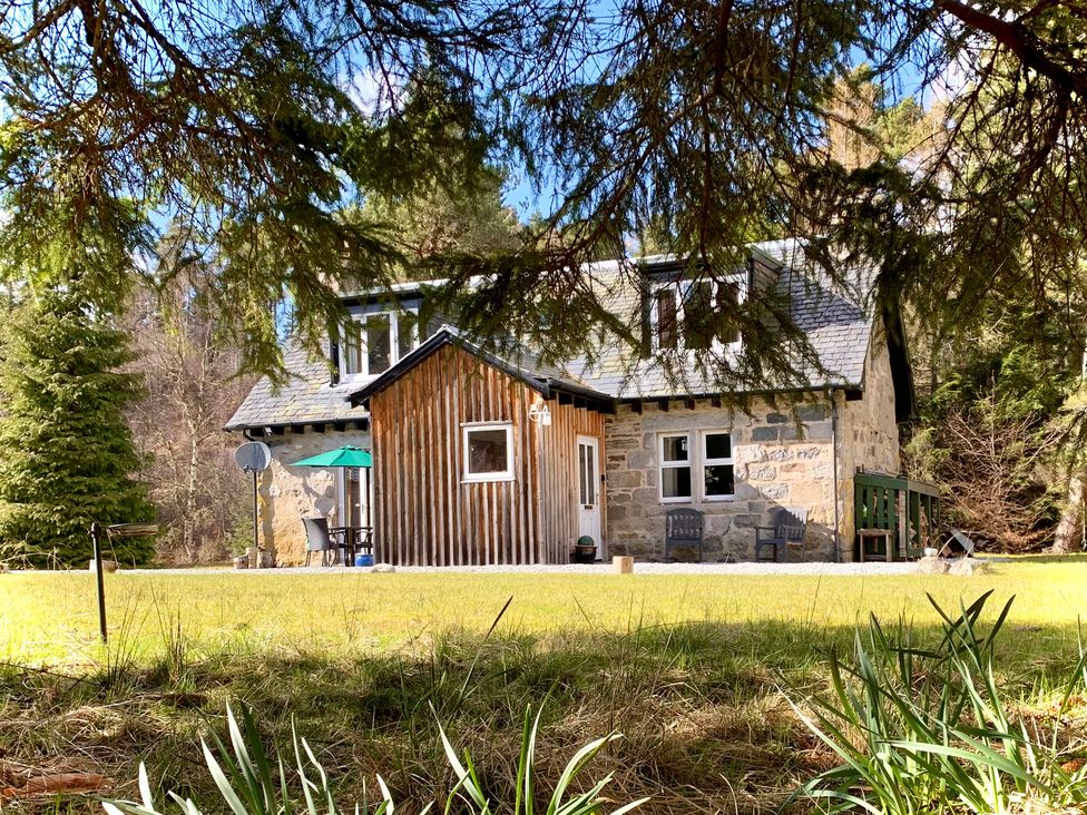 A stone house with a wooden extension surrounded by grass and trees at Feagour in Laggan
