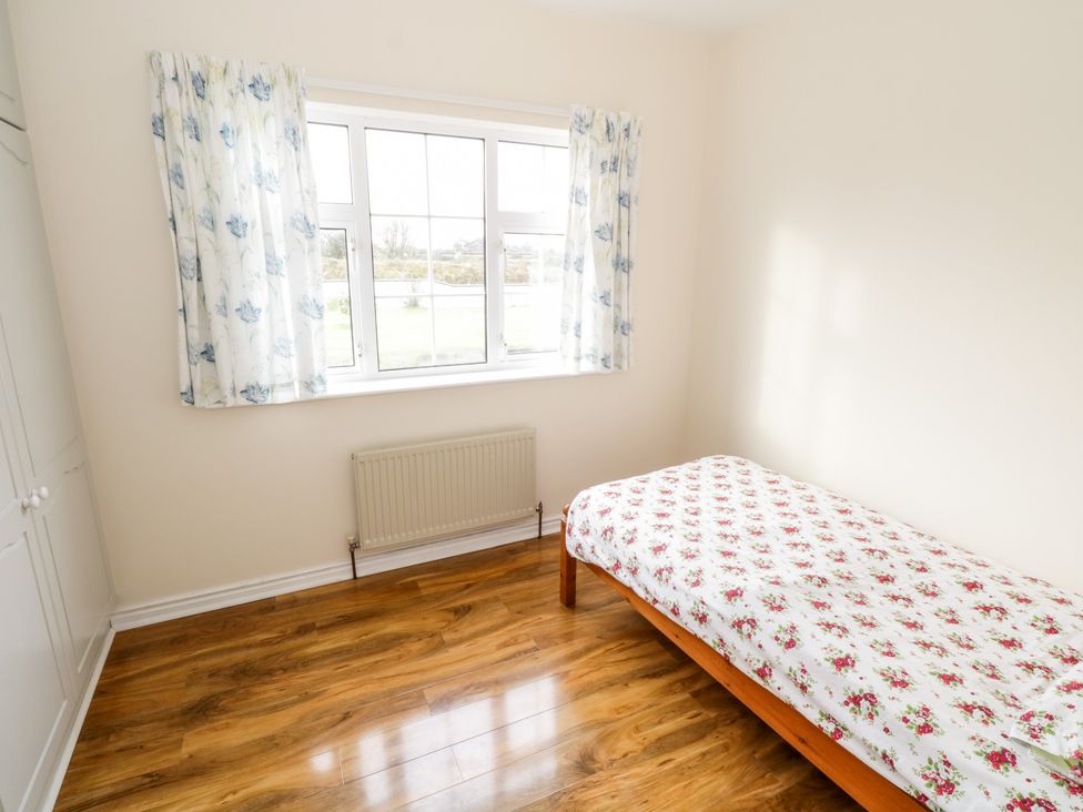 A bedroom with a single bed covered with floral bedding near a window with floral curtains and a built-in wardrobe at Dromore West Cottage in Dromore West County Sligo