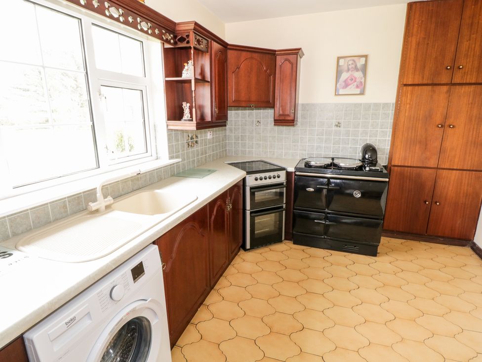 A kitchen with wooden cabinets a washing machine a cream sink an electric stove a black oven a wooden floor and a window at Dromore West Cottage in Dromore West County Sligo