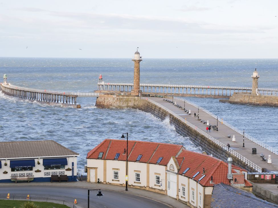 A harbor scene with two lighthouses and a curved pier with people walking by the sea