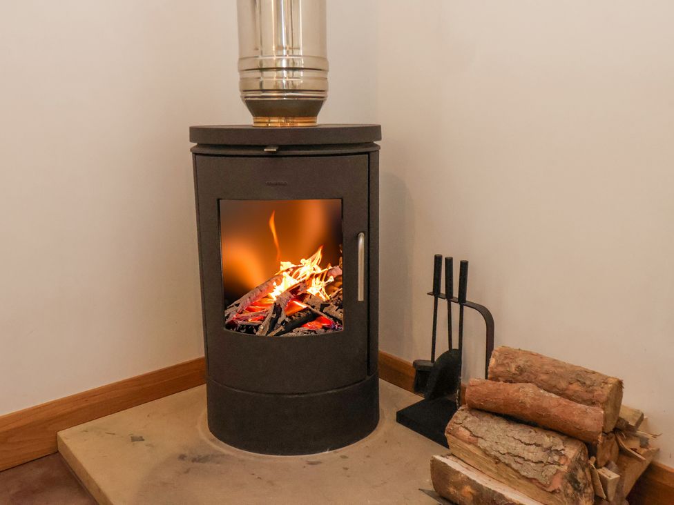 A wood burning stove with firewood and fireplace tools in a corner at Dairy Cottage in Staintondale