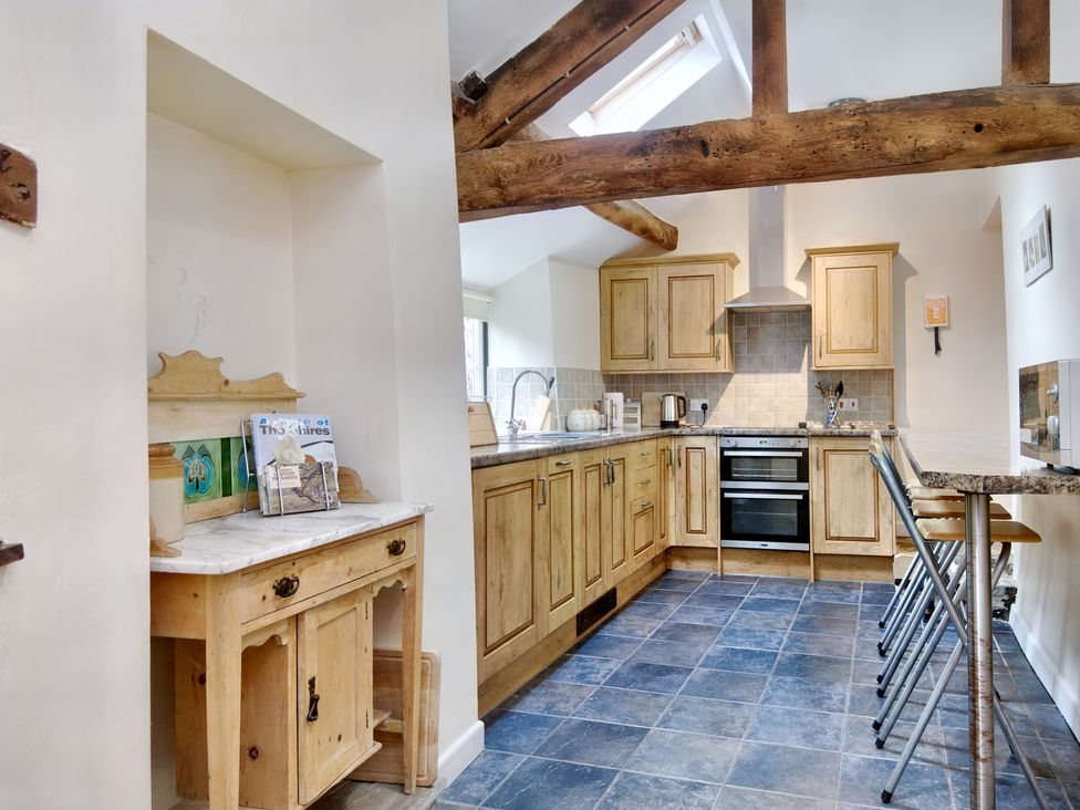 A kitchen with wooden cabinets a tiled floor a small wooden sideboard and a breakfast bar with stools at The Birches in Hay-on-Wye
