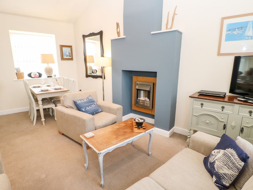 A living room with armchairs a coffee table a fireplace and a dining table in the corner at Driftwood Apartment in Amble-by-the-Sea