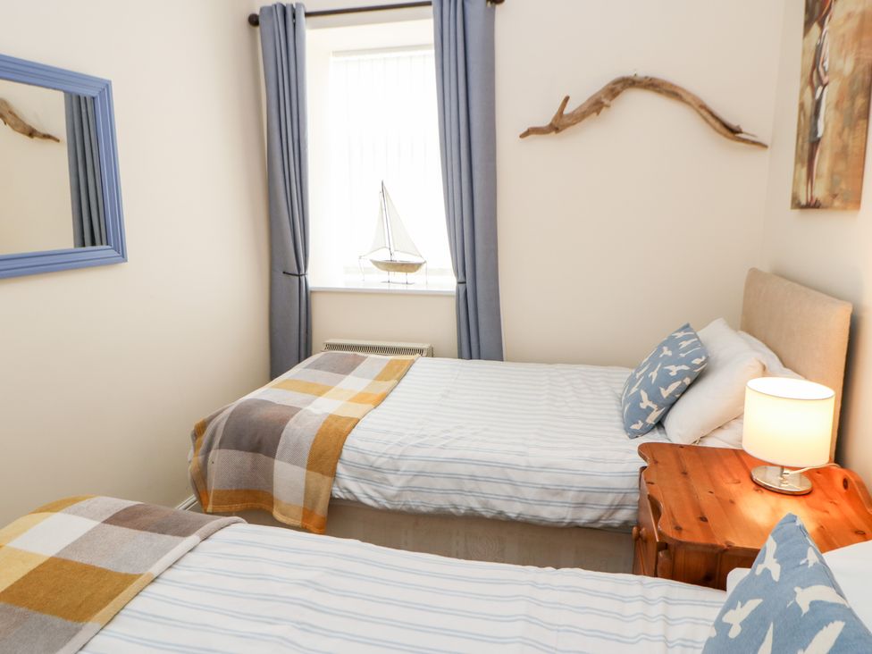 A bedroom with two single beds with checkered blankets and blue bird cushions Driftwood Apartment in Amble-by-the-Sea