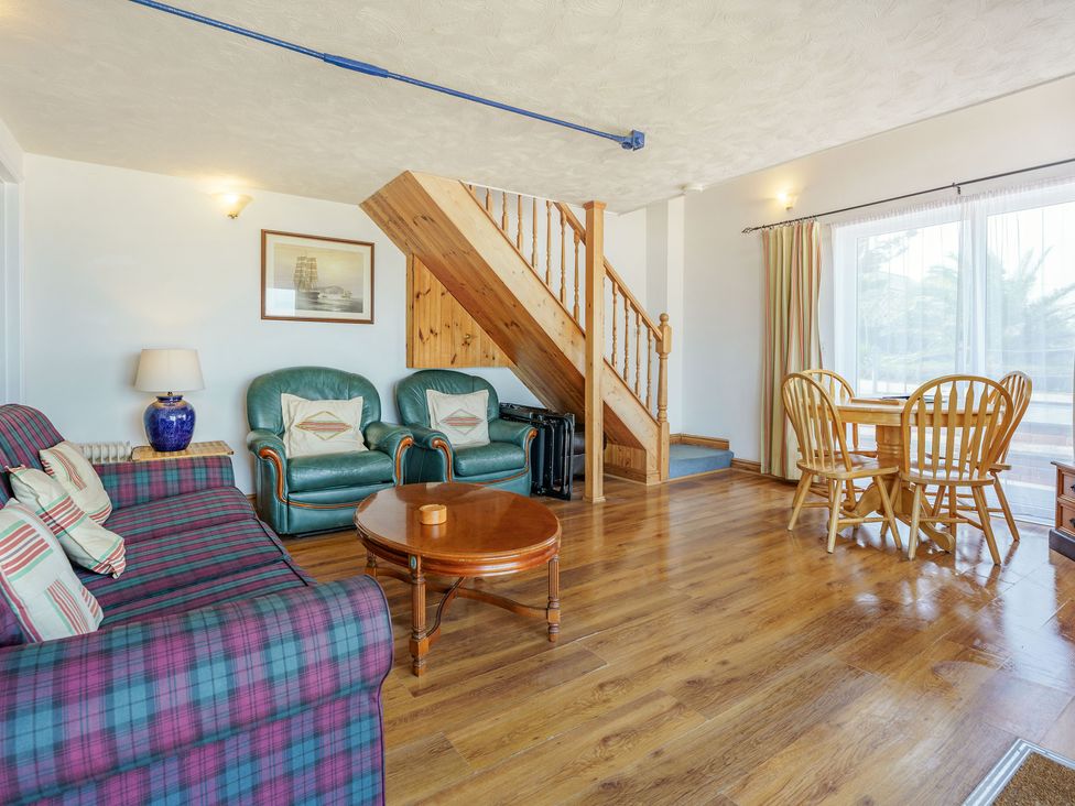 A living room with a plaid sofa green armchairs a wooden coffee table wooden stairs and a dining table with chairs at North West Sea View No 3 in Yarmouth