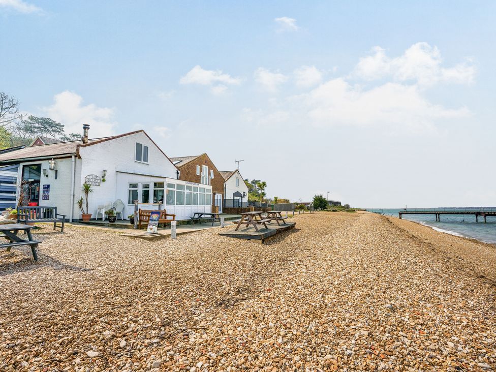 A pebble beach with benches and a white building near the shoreline at North West Sea View No 3 in Yarmouth