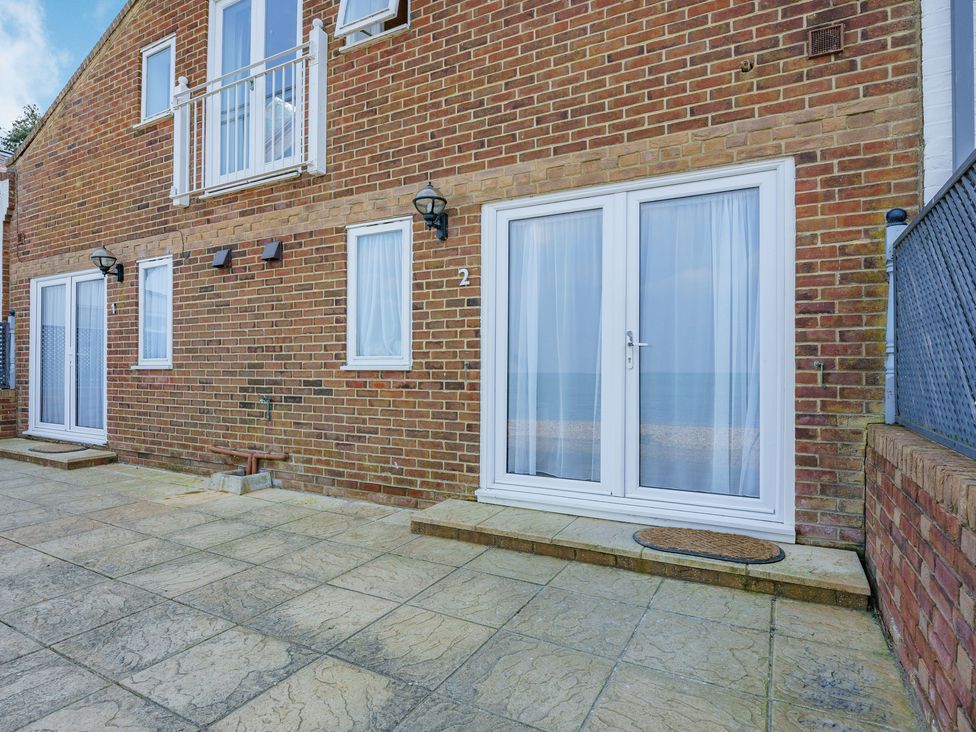 A brick exterior wall with two sets of white double doors and windows above a stone patio at Port Side in Yarmouth