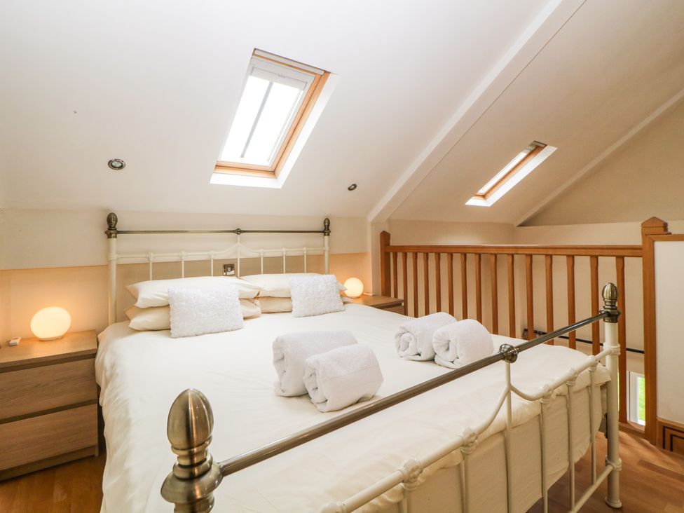 A bedroom with a metal bed frame two bedside tables with lamps skylight windows and rolled towels on the bed at Meader Barn in Peter Tavy near Tavistock
