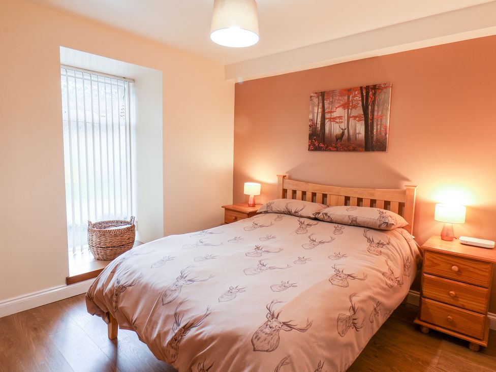 A bedroom with a wooden bed and bedside tables with lamps and a basket on the window ledge at Mulgrave Cottage in Dalehouse near Staithes