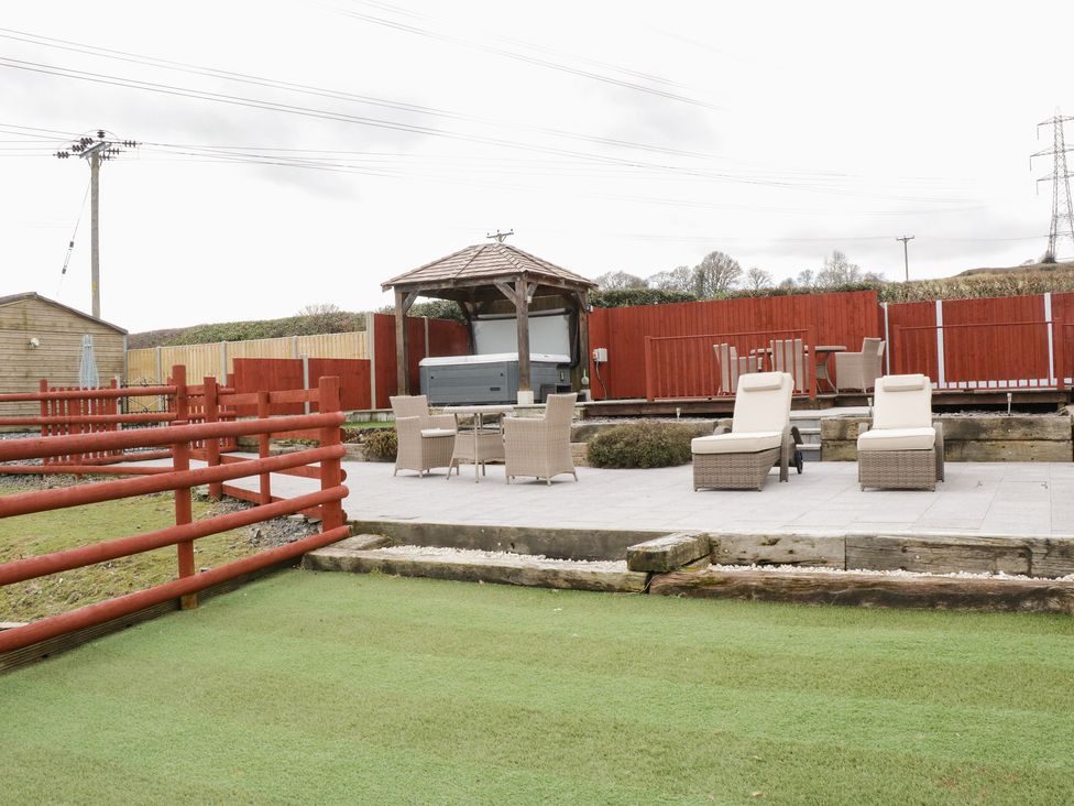 An outdoor patio area with two lounge chairs a table with four chairs a wooden gazebo with a hot tub surrounded by a red wooden fence Bryn Derw Holiday Cottage Eglwysbach near Llanrwst and Conwy