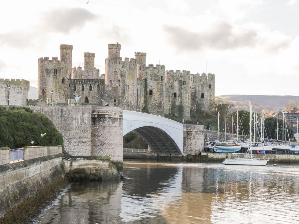 A large stone castle with multiple towers next to a bridge over water with boats docked nearby