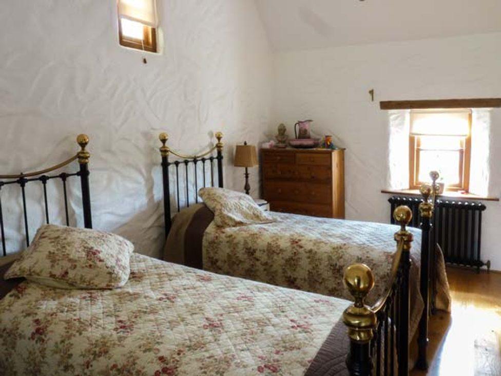 A bedroom with two single beds floral bedspreads a wooden dresser and two windows at Annies Cottage in Doonamona near Belcarra County Mayo