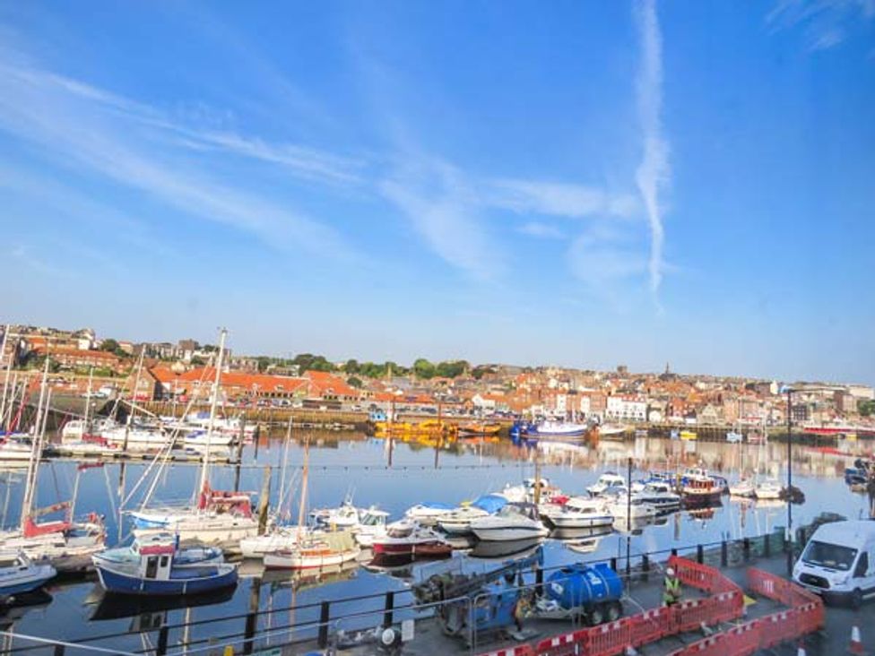 A harbor with boats docked on the water and buildings with orange roofs in the background at Odd Sock Cottage Whitby
