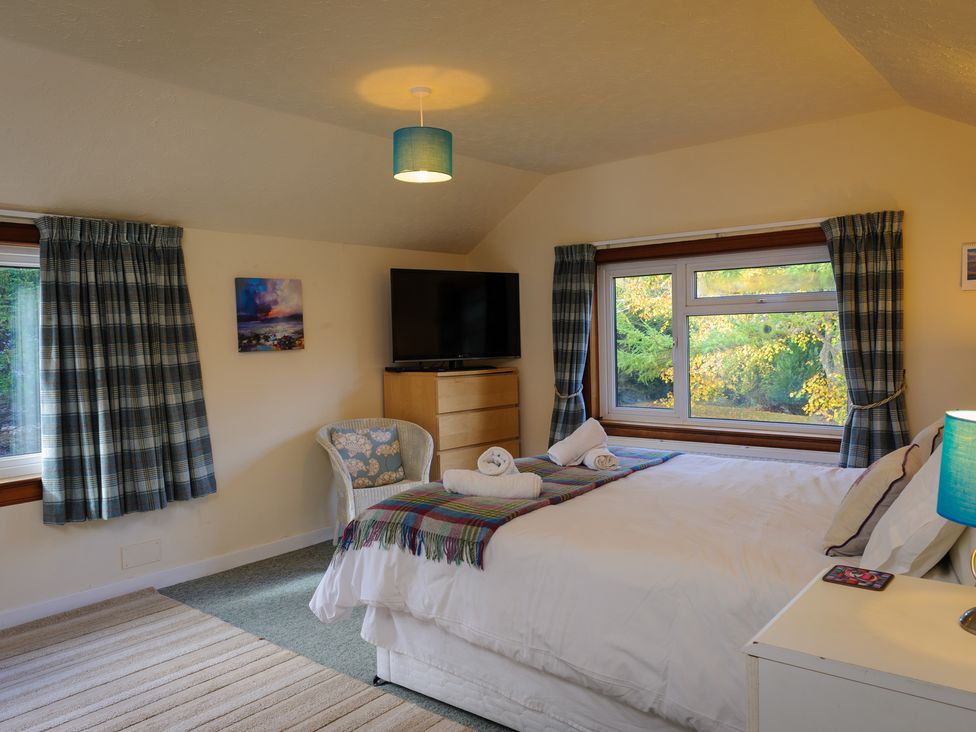 A bedroom with a bed with towels on a blanket and windows with curtains at Alvey House in Newtonmore