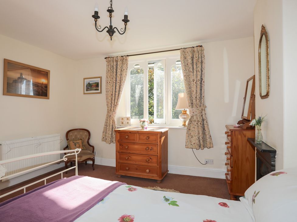 A bedroom with a bed a wooden chest of drawers an armchair framed pictures and a window with curtains at Pabo Lodge in Llandudno Junction near Llandudno