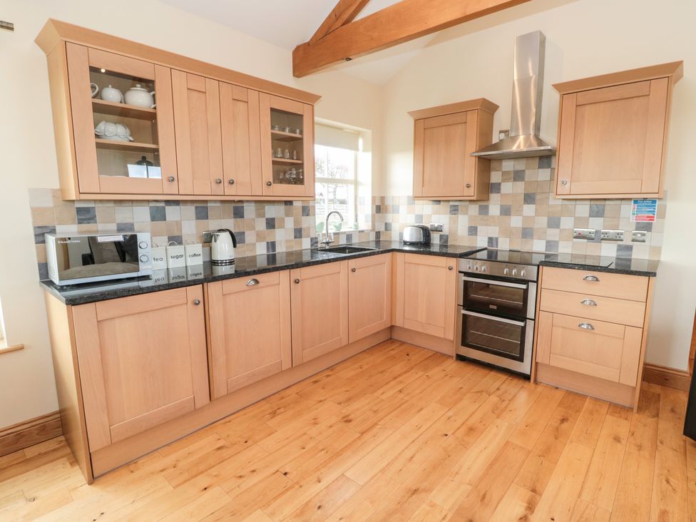 A kitchen with wooden cabinets tiled backsplash and appliances at Bank Top Cottage in Embleton