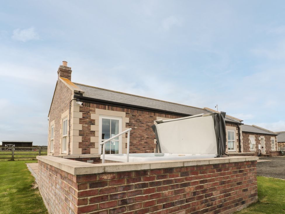 An outdoor hot tub with a cover partially open next to a brick house with windows at Bank Top Cottage in Embleton
