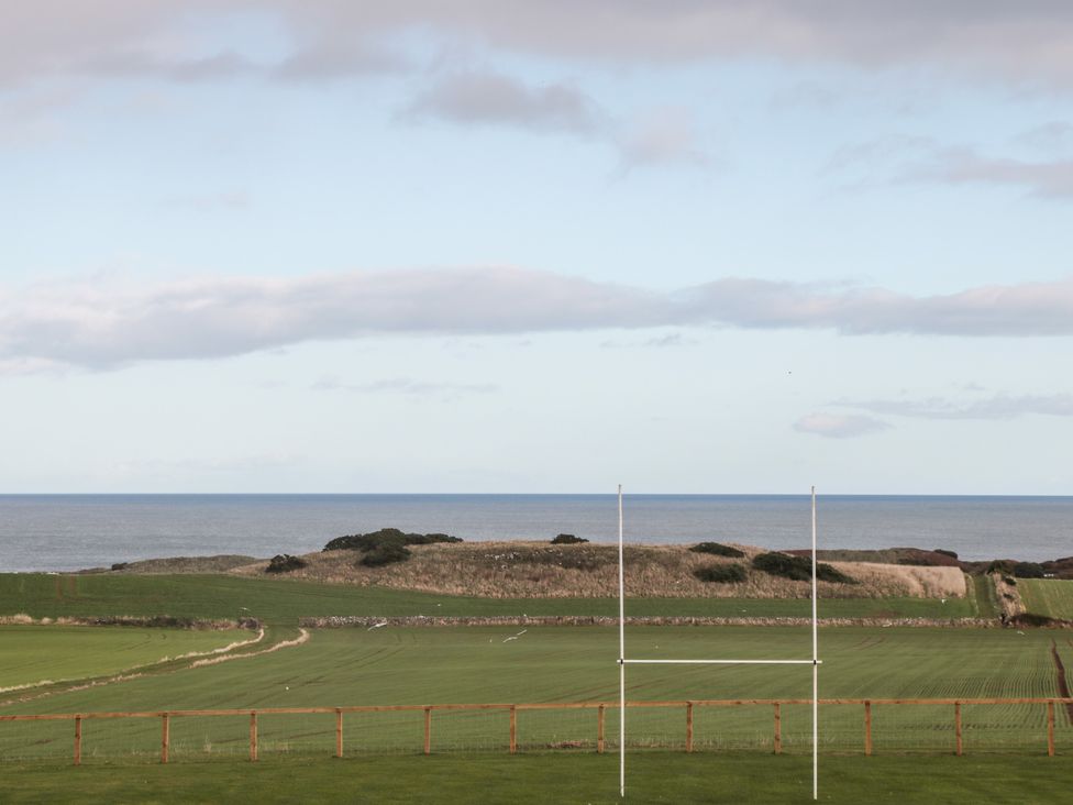 A rugby field with goalposts and a wooden fence overlooking fields and the sea at Bank Top Cottage in Embleton