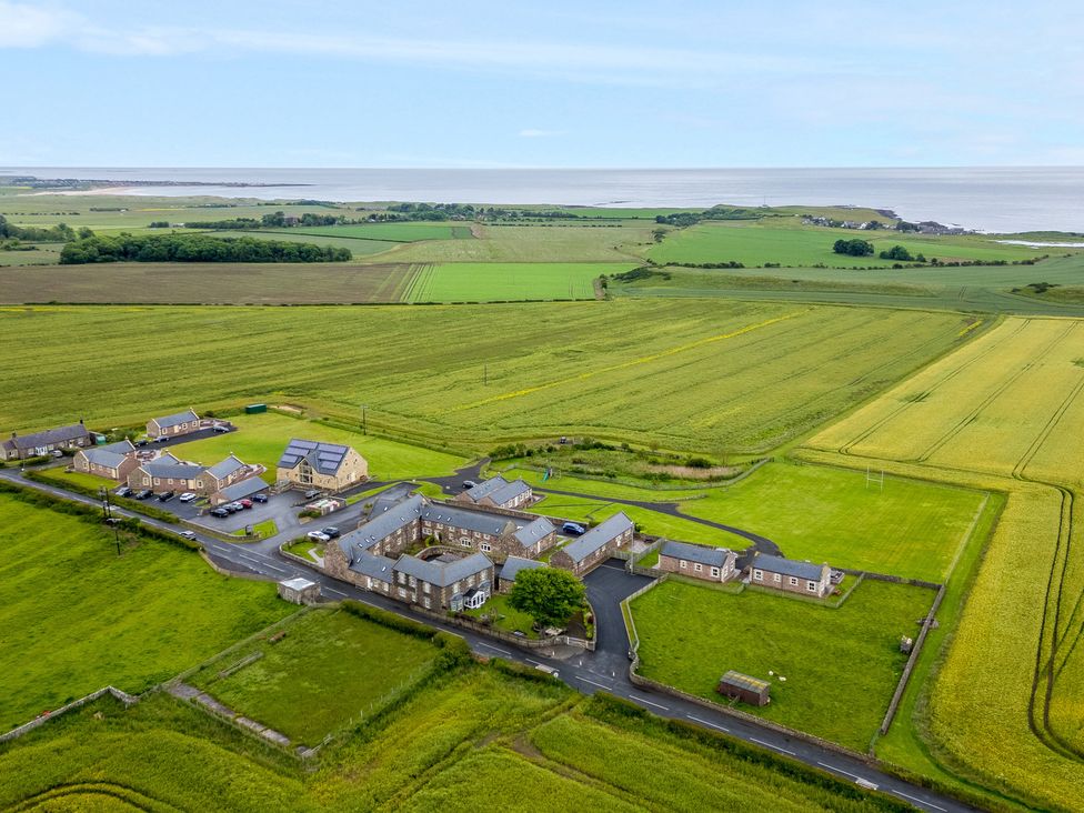 An aerial view of a countryside property with multiple stone buildings a parking area surrounding green fields and the sea in the distance at Bank Top Cottage in Embleton