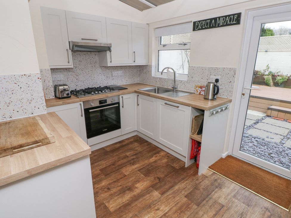 A kitchen with white cabinets wooden countertops a gas stove oven toaster kettle a window and a door to patio at Bank House in Capel Iwan near Newcastle Emlyn
