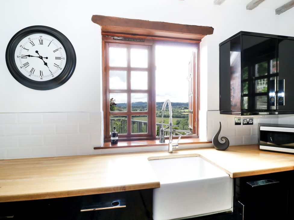 A kitchen with wooden countertops a white sink a window with a view and a clock on the wall at Hillview Cottage in Knightwick near Worcester