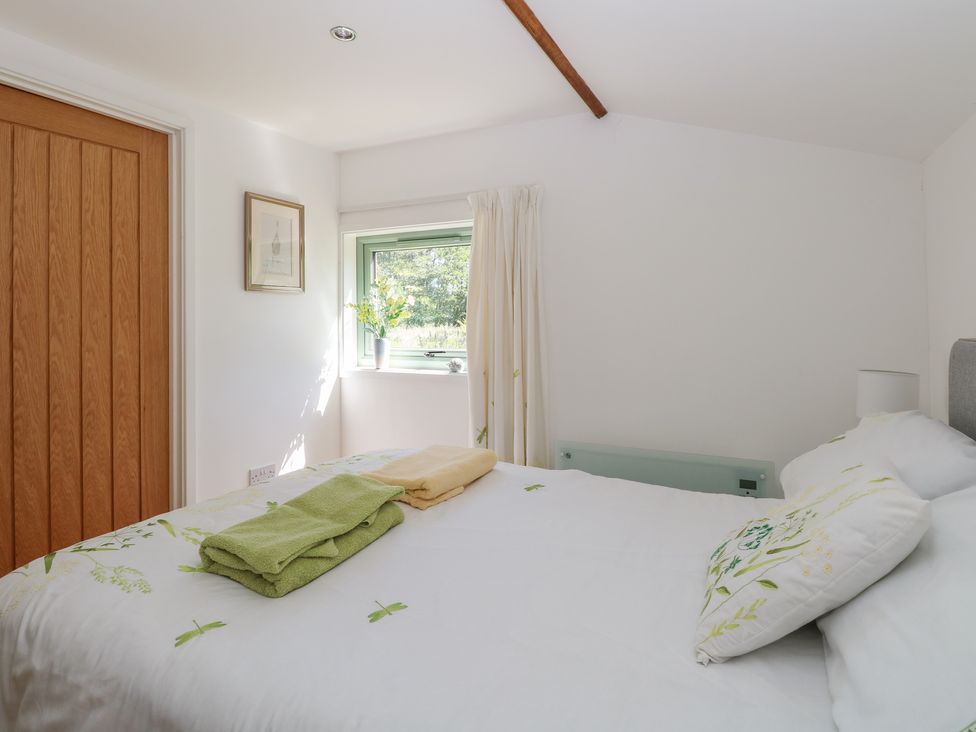 A bedroom with a bed with folded towels on it a small window with a vase of flowers and a wooden door at Lakeside Lodge in East Harling near Thetford