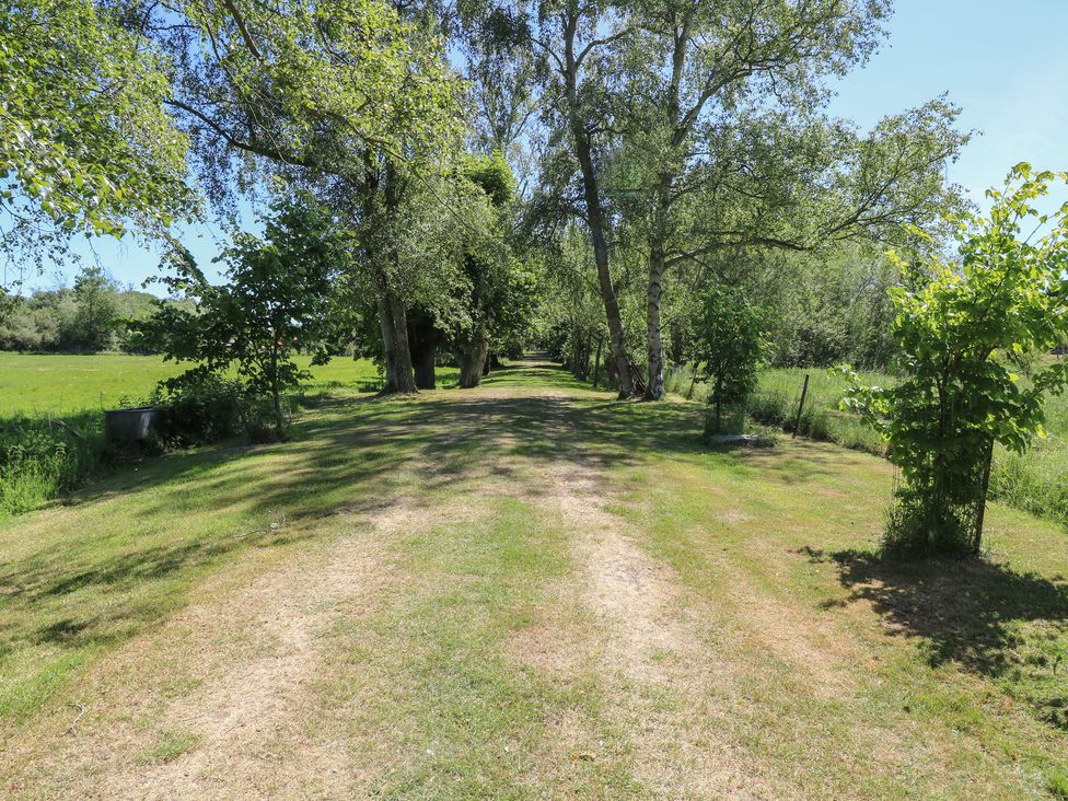 A grassy path lined with trees and bushes on both sides at Lakeside Lodge in East Harling near Thetford